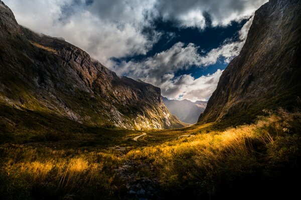 Strada tra montagne con nuvole e sole