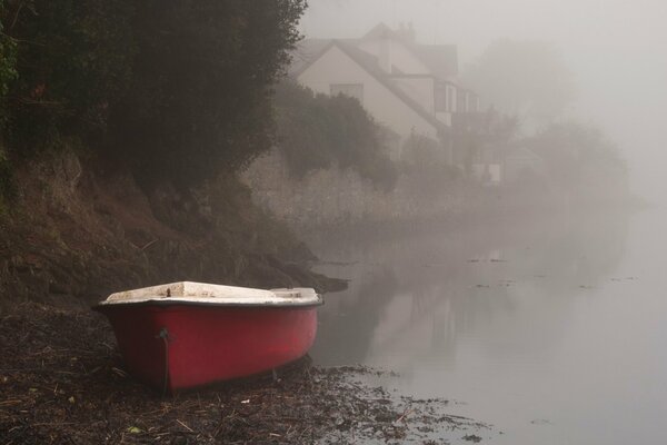 Rive de la rivière brumeuse avec un bateau rouge