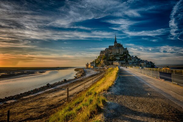 Schloss der Insel Mont-Saint-Michel in der Abendsonne unter blauem Himmel mit Wolken