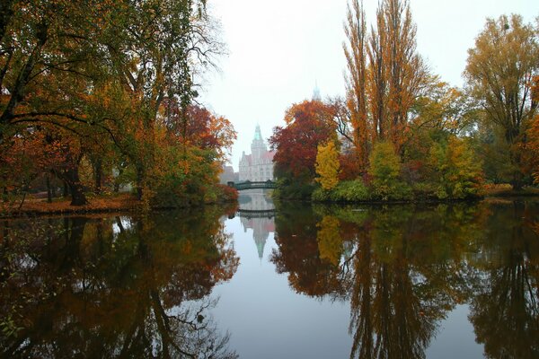 Autumn landscape with a river next to which you can see a bridge and a tall building