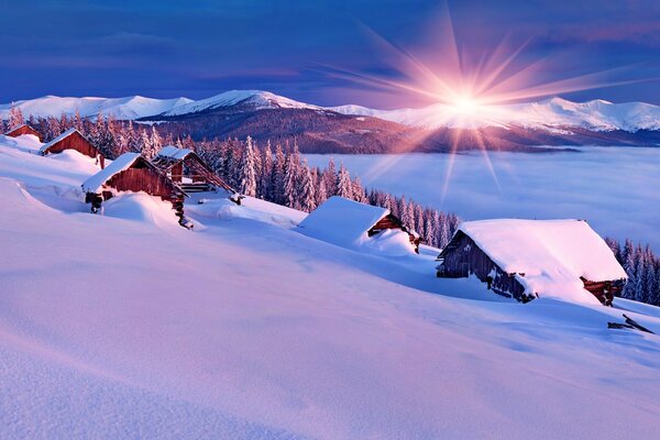 Sonnenaufgang in den Bergen mit Häusern im Schnee am Hang