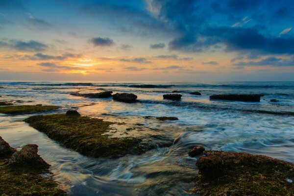 Las olas golpean las rocas y el sol se abre paso a través de las nubes