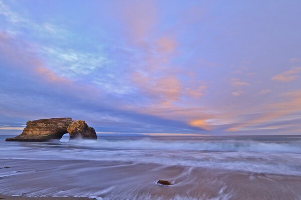 Surf of blue waves with white sea foam, with rare rocks near the shore