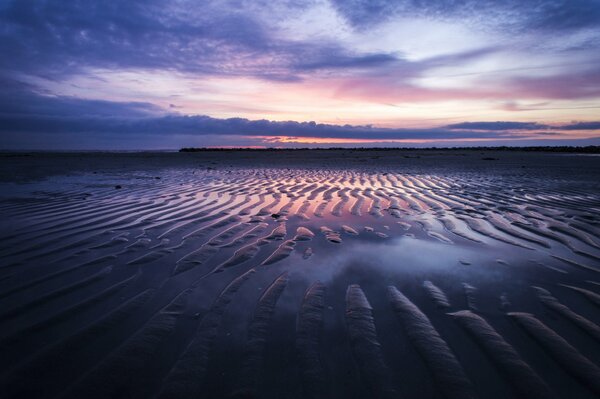 A beach with dunes at low tide against a sunset cloudy sky