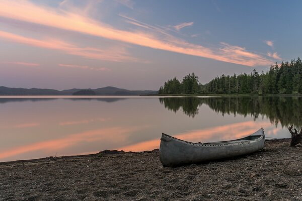 El bosque se refleja en el agua y en la orilla hay un barco