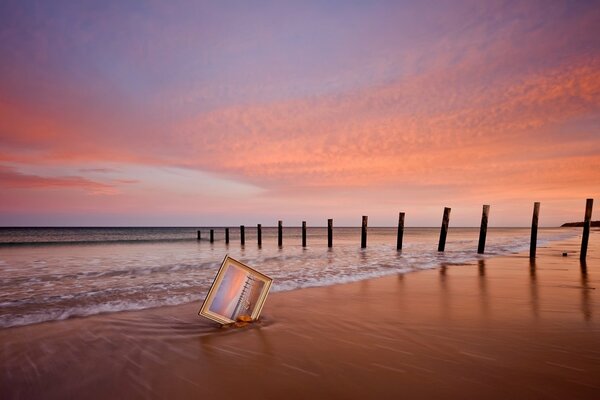 A picture in the sand by the sea against a pink sky