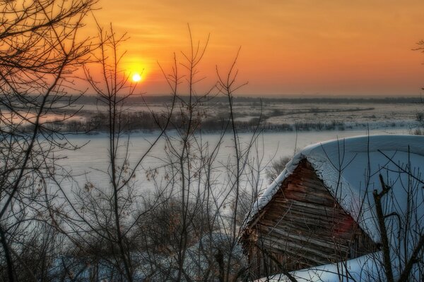 Puesta de sol sobre el bosque de invierno y la cabaña