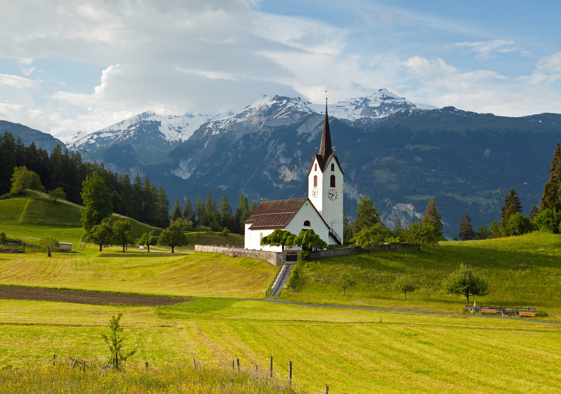 reines grisons suisse alpes montagnes sommets pré herbe arbres église ciel nuages