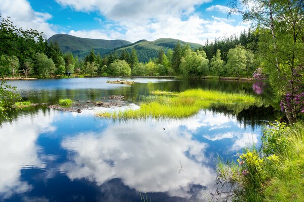 Weiße Wolken spiegeln sich in den Seen Schottlands auf dem Hintergrund von grünen Bäumen wider