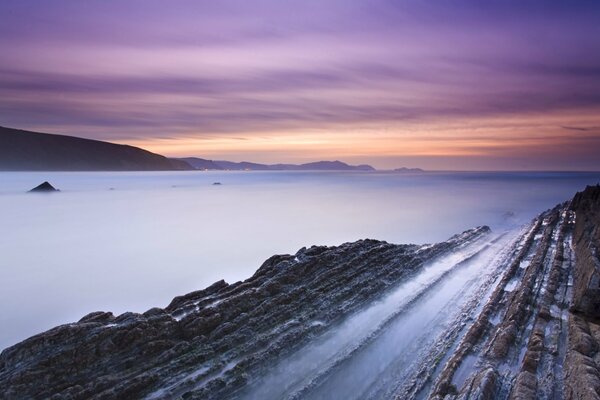 Costa rocosa de la bahía en España, en medio de una puesta de sol naranja