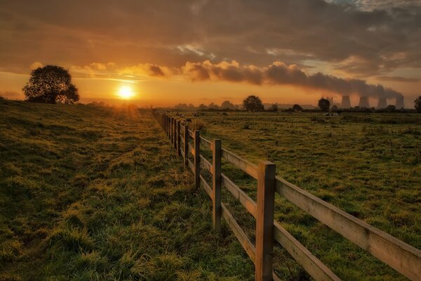 Untergehende Sonne über einem Feld mit einem Zaun