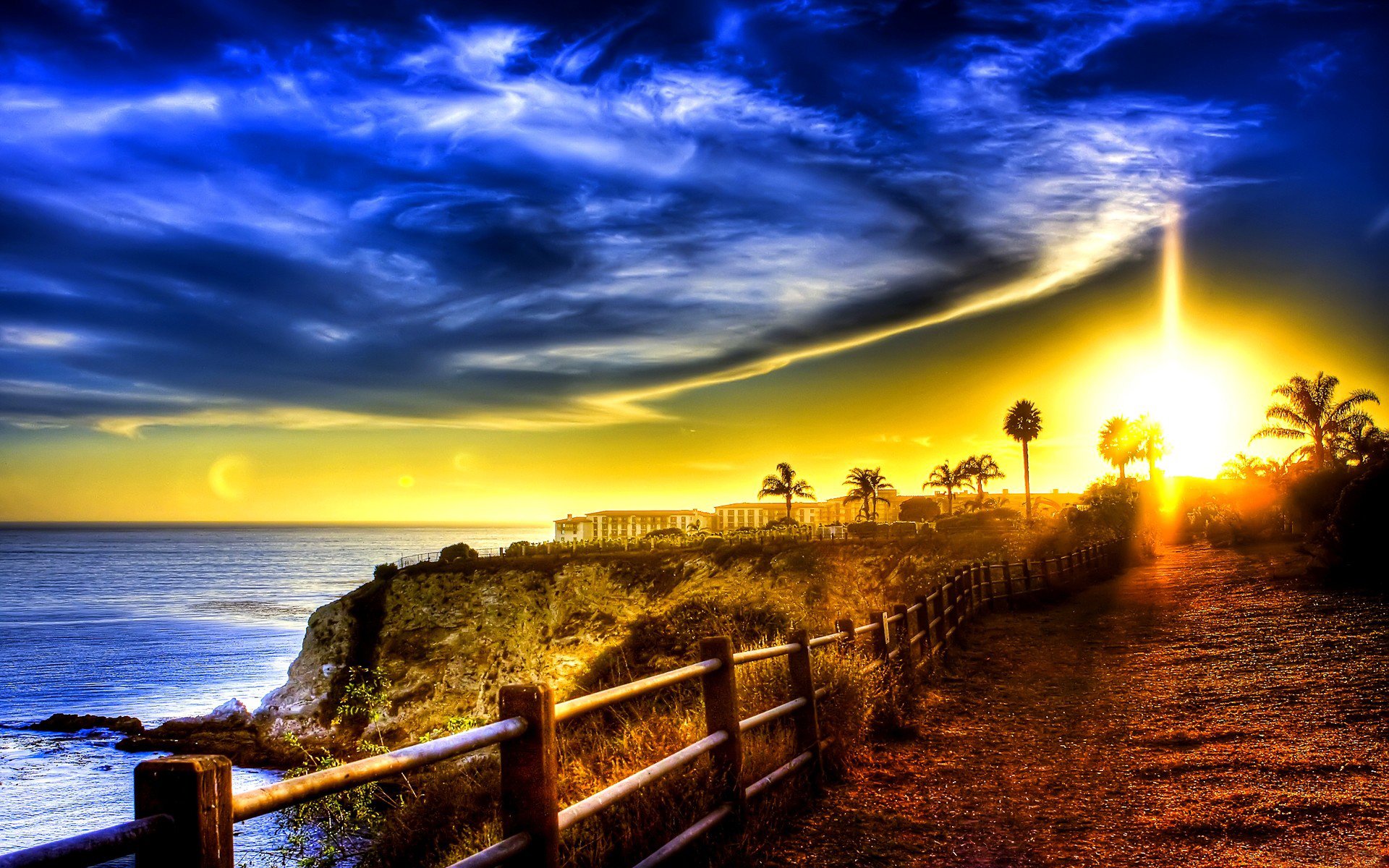 ea ocean coast buildings road fence palm sky clouds dawn sunset rays light