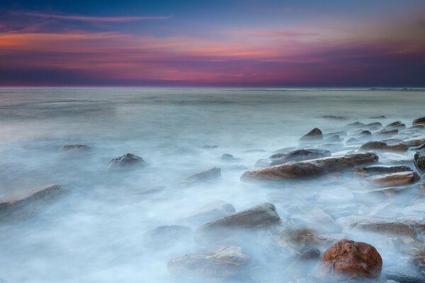 Mar tranquilo con piedras y hermosa puesta de sol