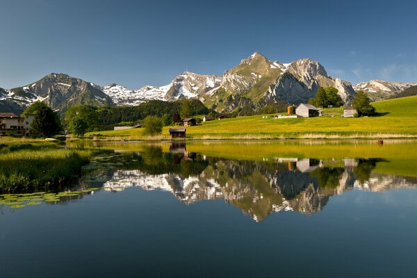 A green meadow and a lake in which the mountains are reflected