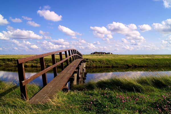 A wooden bridge over a small river connects two fields