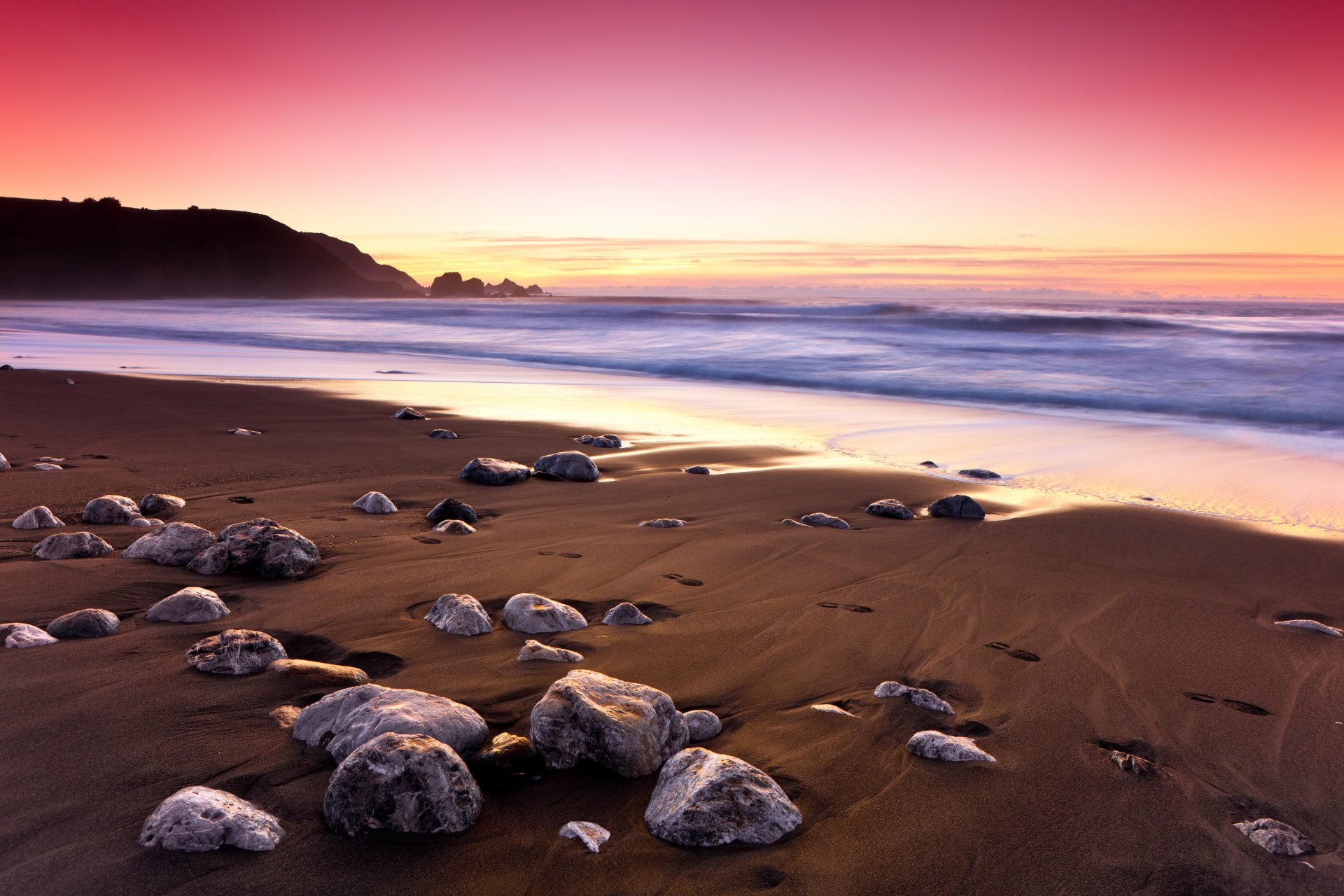 puesta de sol océano roca costa piedras arena huellas