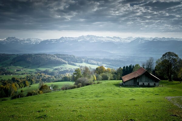 Maison sur une colline verdoyante. Montagnes à l horizon