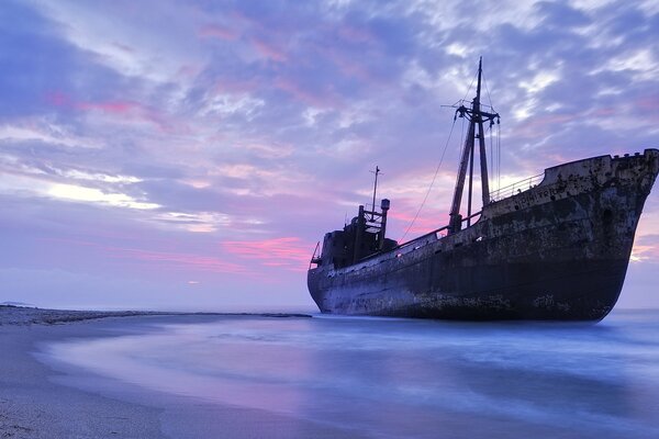 Altes Schiff am Sandstrand bei Sonnenuntergang