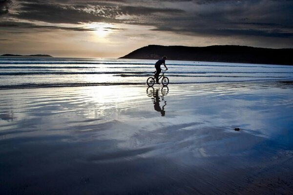 A cyclist rides on the water on the seashore