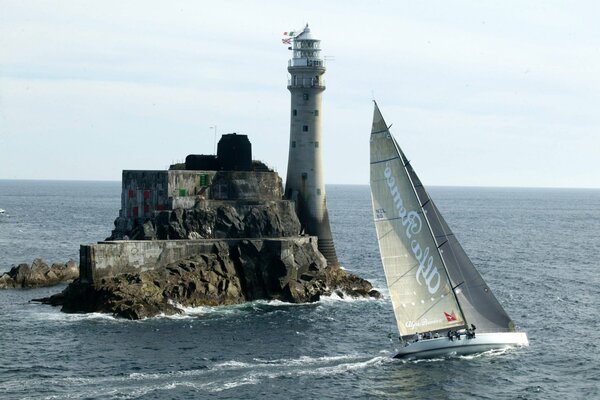 The yacht sails past the lighthouse on the rock