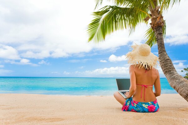 A girl writes an article in a laptop sitting by the sea