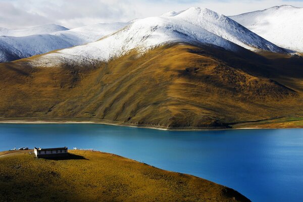 Casa solitaria in riva al fiume sullo sfondo delle montagne innevate del Tibet