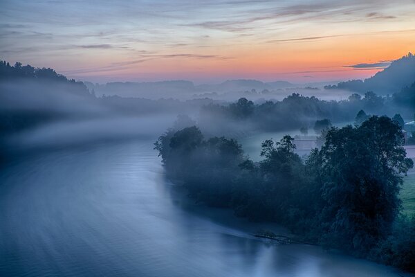 Letto del fiume avvolto dalla nebbia sullo sfondo delle montagne