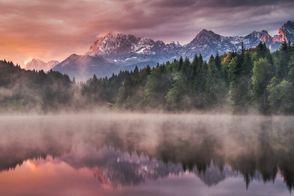 Nebel über dem Waldsee. Berge im Hintergrund