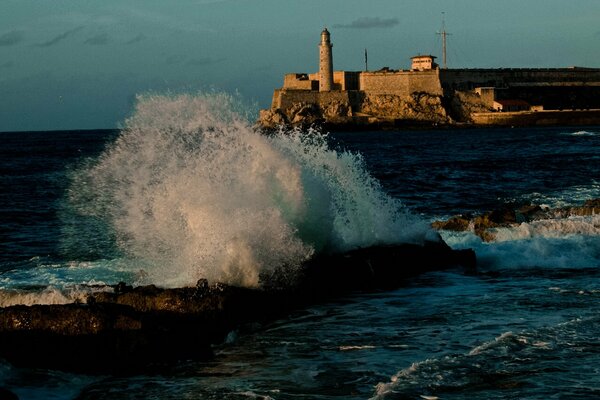 Spruzzi di onde sul mare con un faro in lontananza