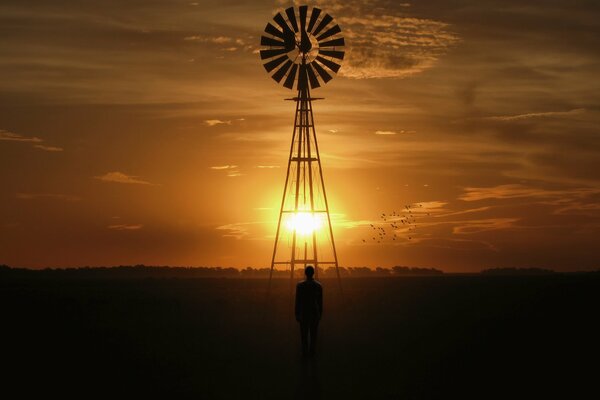 Uomo e mulino a vento sullo sfondo del cielo al tramonto