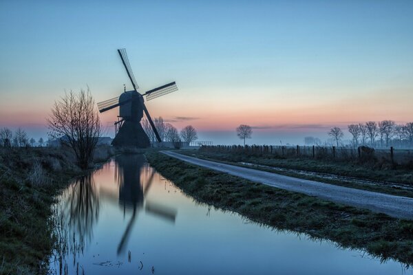 Moulin à vent et route près de l eau, sur fond de coucher de soleil