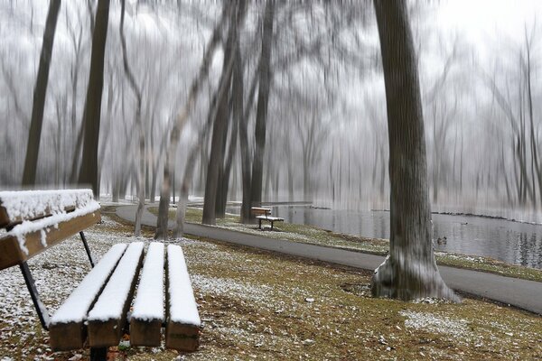 A snow-covered bench in the park near the pond