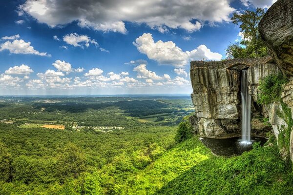 Hohe Klippen. Ein Wasserfall aus Felsen. Grünes Tal und blauer Himmel mit weißen Wolken