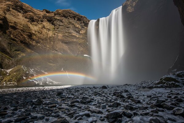 Waterfall and rainbow on blue sky background