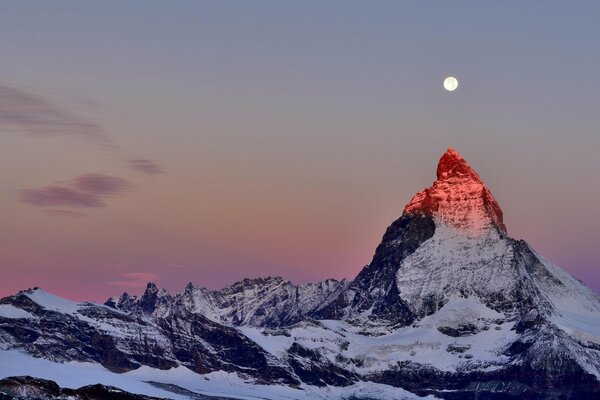 The top of the Alps against the twilight sky. Moon over the top