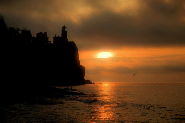 Puesta de sol en el mar junto a un acantilado con un faro