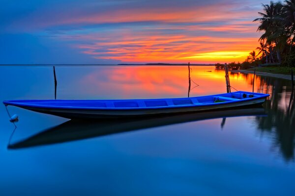 A long boat on the calm surface of the water against the background of palm trees and sunset