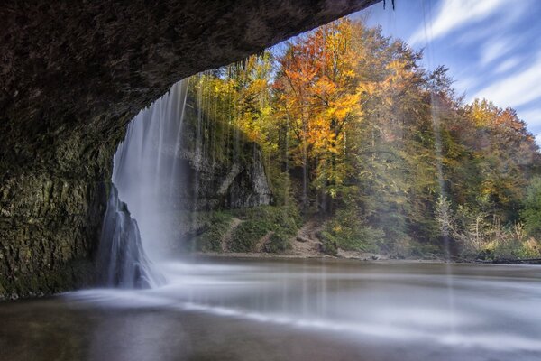 En otoño, una cascada cae desde un acantilado en un lago