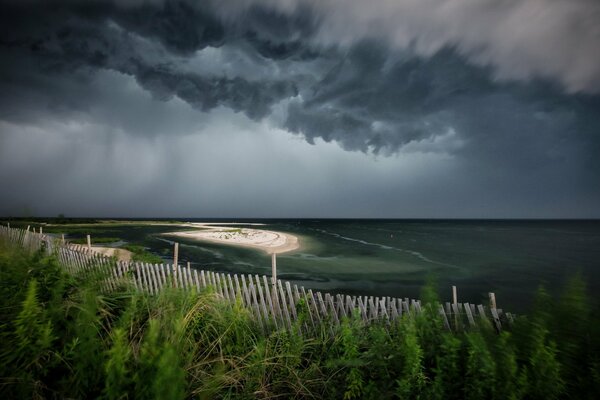 Die Natur bereitet sich auf den Schlaf vor: das Meer, der Zaun am Ufer und die Wolken am Himmel