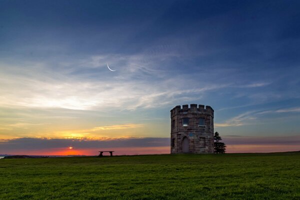 Bei Sonnenuntergang werden ein Feld und eine Bank mit einem Turm fotografiert