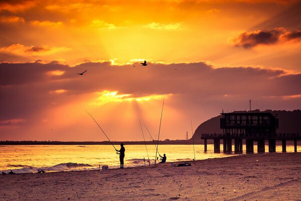 Puesta de sol en la orilla del mar. Hombre pescando en la orilla