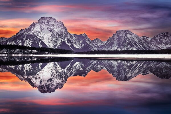 The amazing colors of the departing sun are reflected in the water at the foot of the mountains in the Grand Teton National Park USA