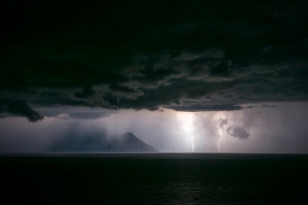 Ein Blitz aus Wolken schlägt in den Ozean neben der Insel. Riesige schwarze Wolken