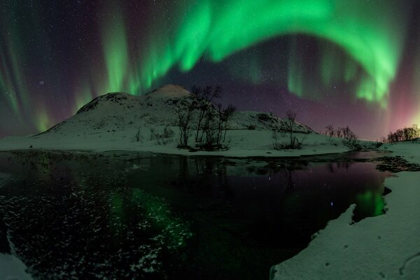 The idyll of the northern lights in the night haze with reflection in the water in green tones