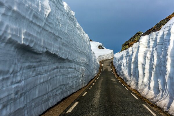 Der Weg, der in die Ferne unter den schneebedeckten Bergfelsen führt