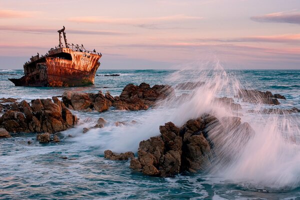 A ship among the sea and rocks on the background of sunset