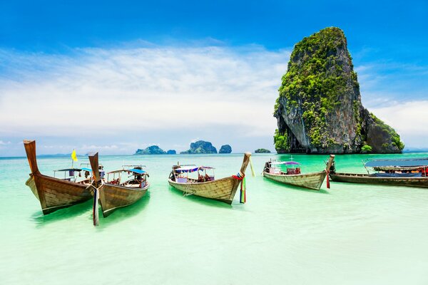The boats are on the shore of the emerald ocean and a large rock