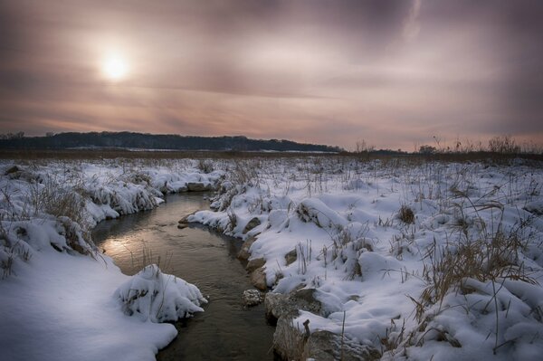 Winter field. The river between the snowdrifts