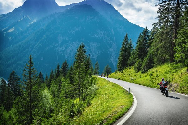 Un motociclista recorre una pista de montaña entre montañas verdes